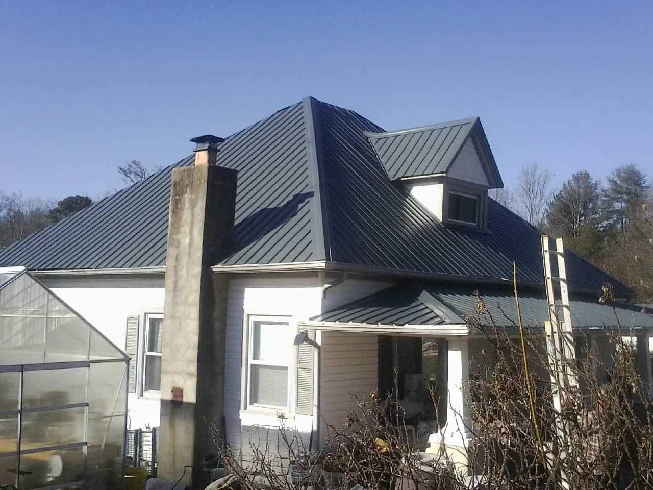 Dark blue standing seam metal roof on a white farmhouse with dormer — Slate & Tile Roof Repair by Roofing Brothers in Abercrombie