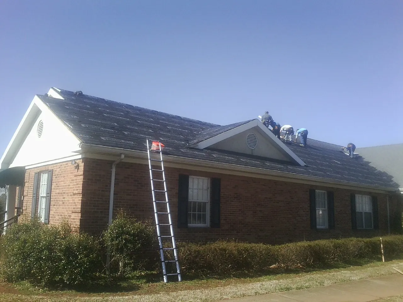 Crew tearing shingles off a brick ranch roof with a ladder set — Metal Roof Repair work by our crew in Abercrombie