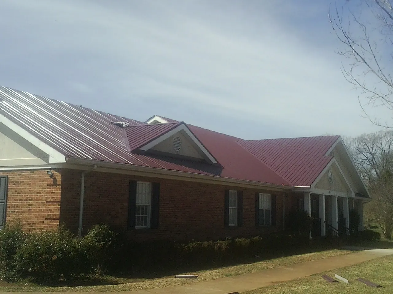 Red metal roof with gabled entries on a long brick building, from a Hail Damage Roof Repair job in Abercrombie