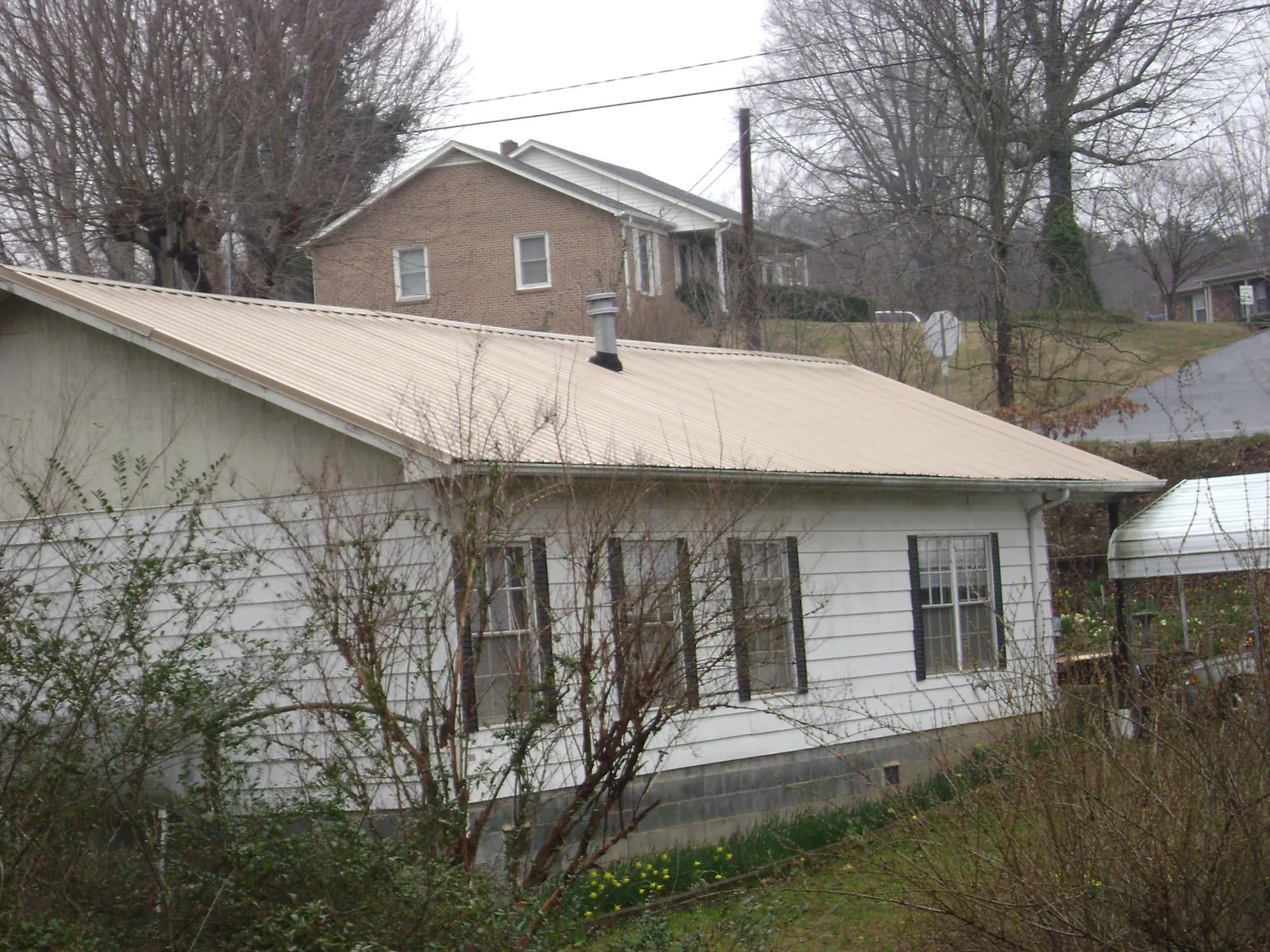 Tan metal roof on a white sided house set into a hillside — Commercial Roofing by Roofing Brothers in Abercrombie